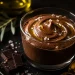 Mousse de chocolate negro aveludada servida num copo de vidro elegante, finalizada com flor de sal e um fio de Azeite Invictus Biológico para um brilho luxuoso.