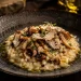 Prato de risotto de cogumelos silvestres com lascas de queijo e trufa, finalizado com um círculo de Azeite Invictus Premium dourado, realçando a textura cremosa.