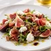 Salada colorida de figos frescos, fatias de presunto ibérico e queijo de cabra, temperada com Azeite Invictus Biológico, apresentada de forma minimalista.